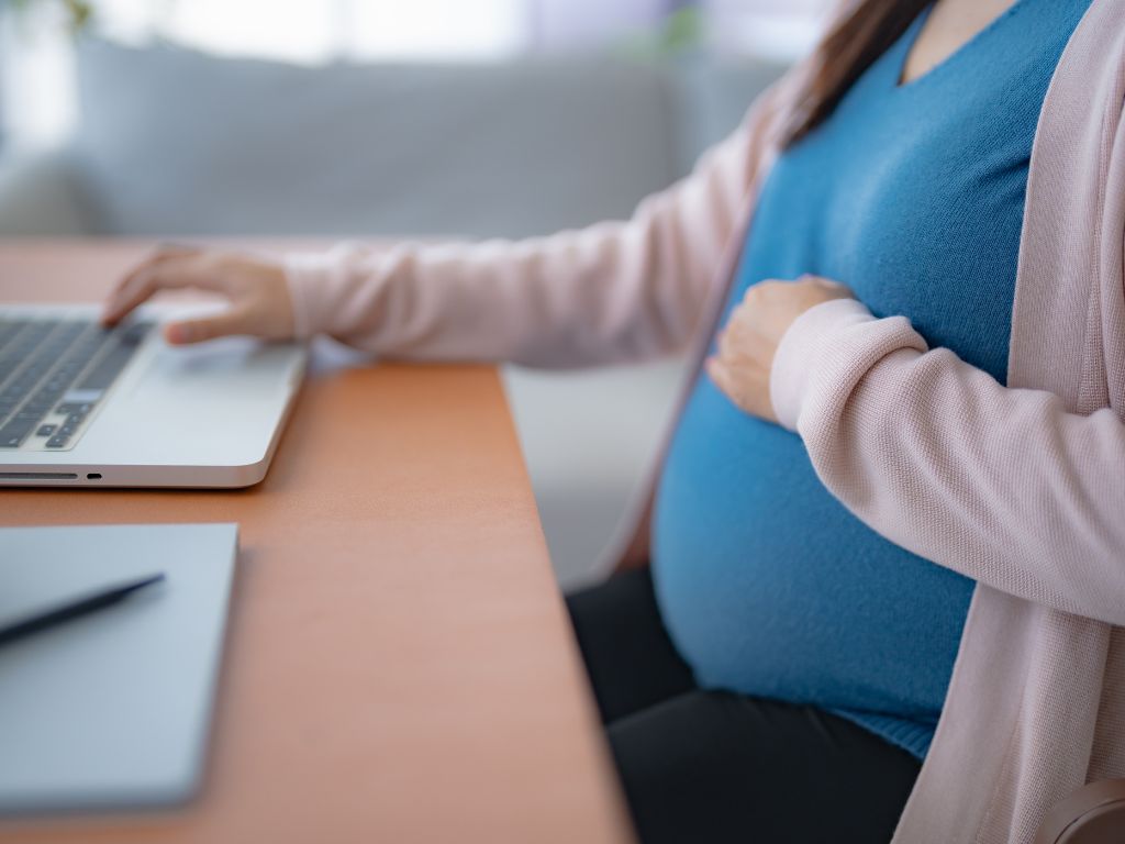 ノートパソコンで仕事をしながらお腹に手を添える妊娠中の女性